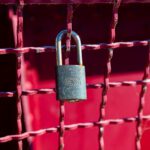 brass padlock on red metal fence